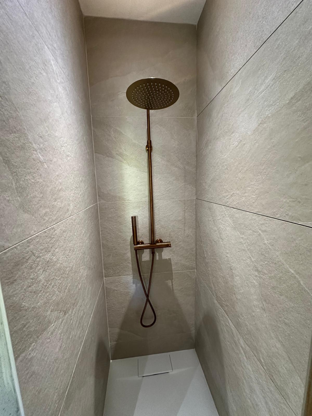 Douche au carrelage clair et à la robinetterie dorée, réalisée par Passalacqua Plomberie.